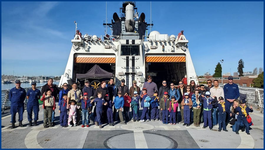 A number of adults and uniformed scouts standing in front of helicopter hangers on the deck of a Coast Guard Cutter