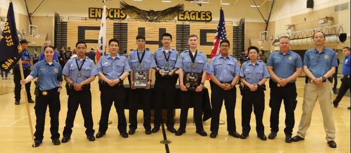 10 scouts and 2 adults all wearing law enforcement uniforms, standing at attention and hold plaques and flags